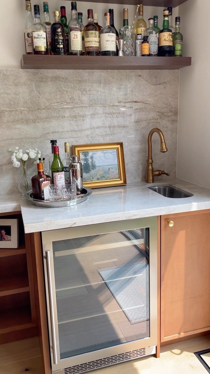 Home wet bar with marble countertop, small sink, beverage cooler, and liquor shelf.