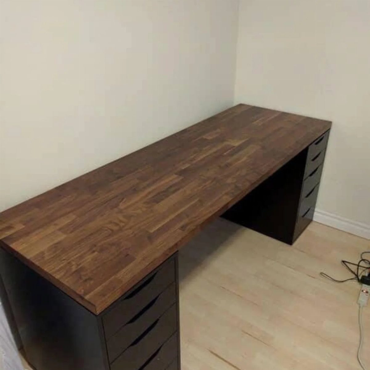 Butcher block desk top resting on two black drawer units in a room.