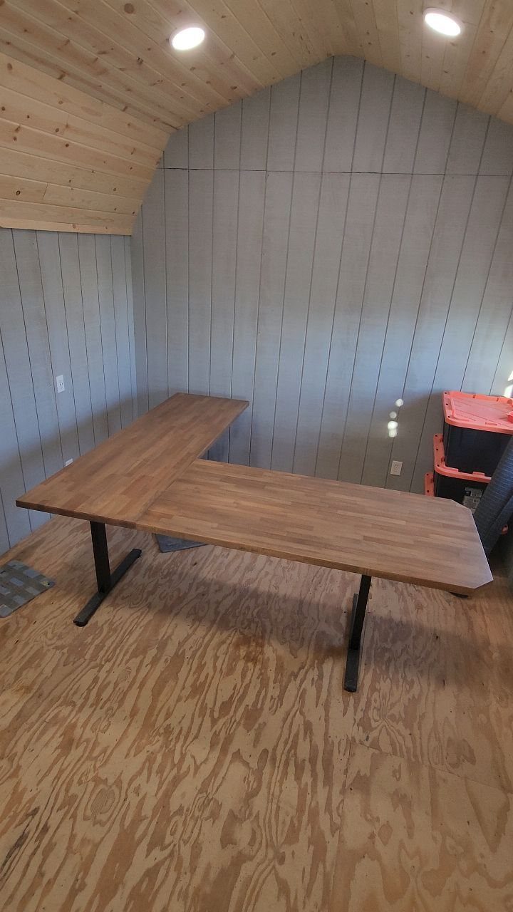 L-shaped butcher block desk with black metal legs in a wood-paneled room