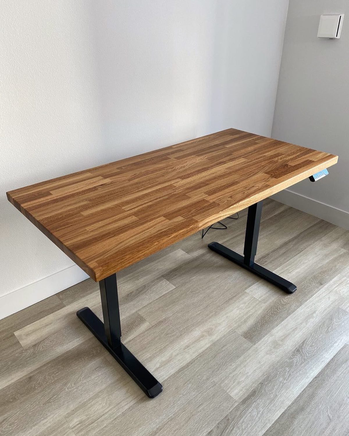 Butcher block desk with black metal legs against a white wall and grey floor