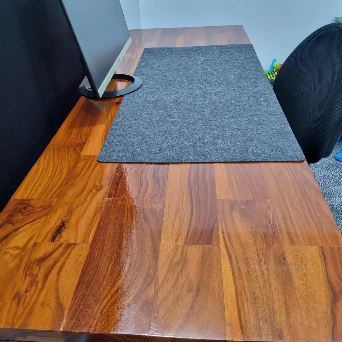 Polished brown butcher block desk with a grey felt mat and computer monitor.