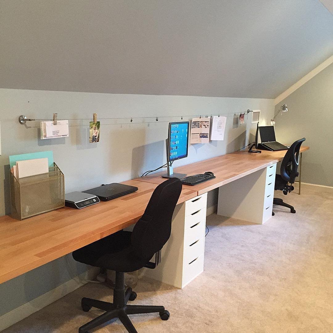 Long butcher block desk with white drawers and black chairs in home office