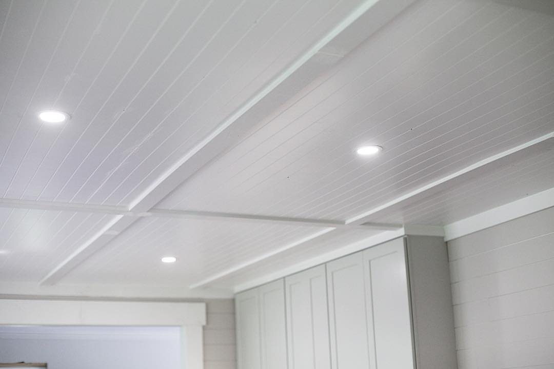White beadboard ceiling with recessed lights and structural beams in a bright room.