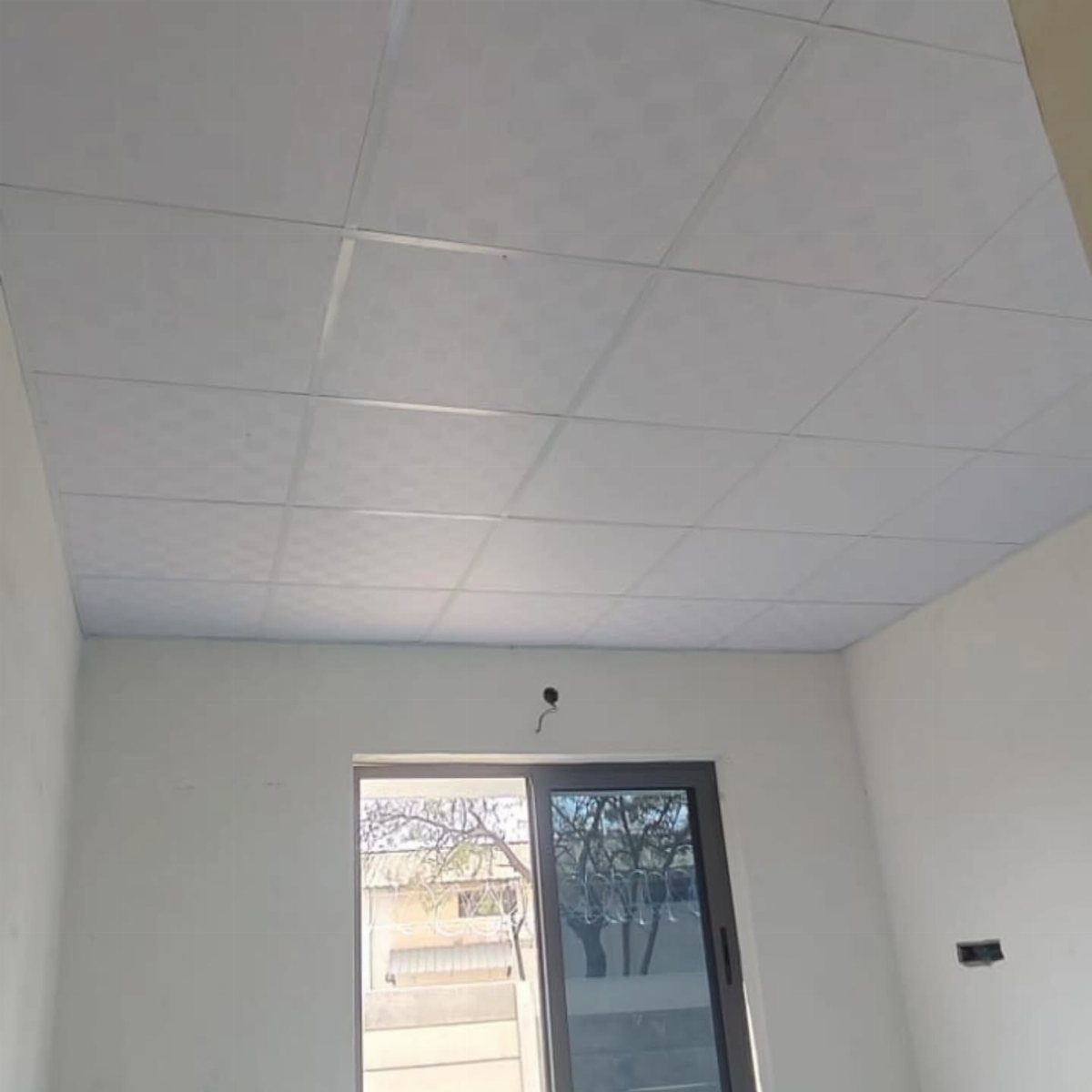 White suspended grid ceiling with textured square tiles in an empty room
