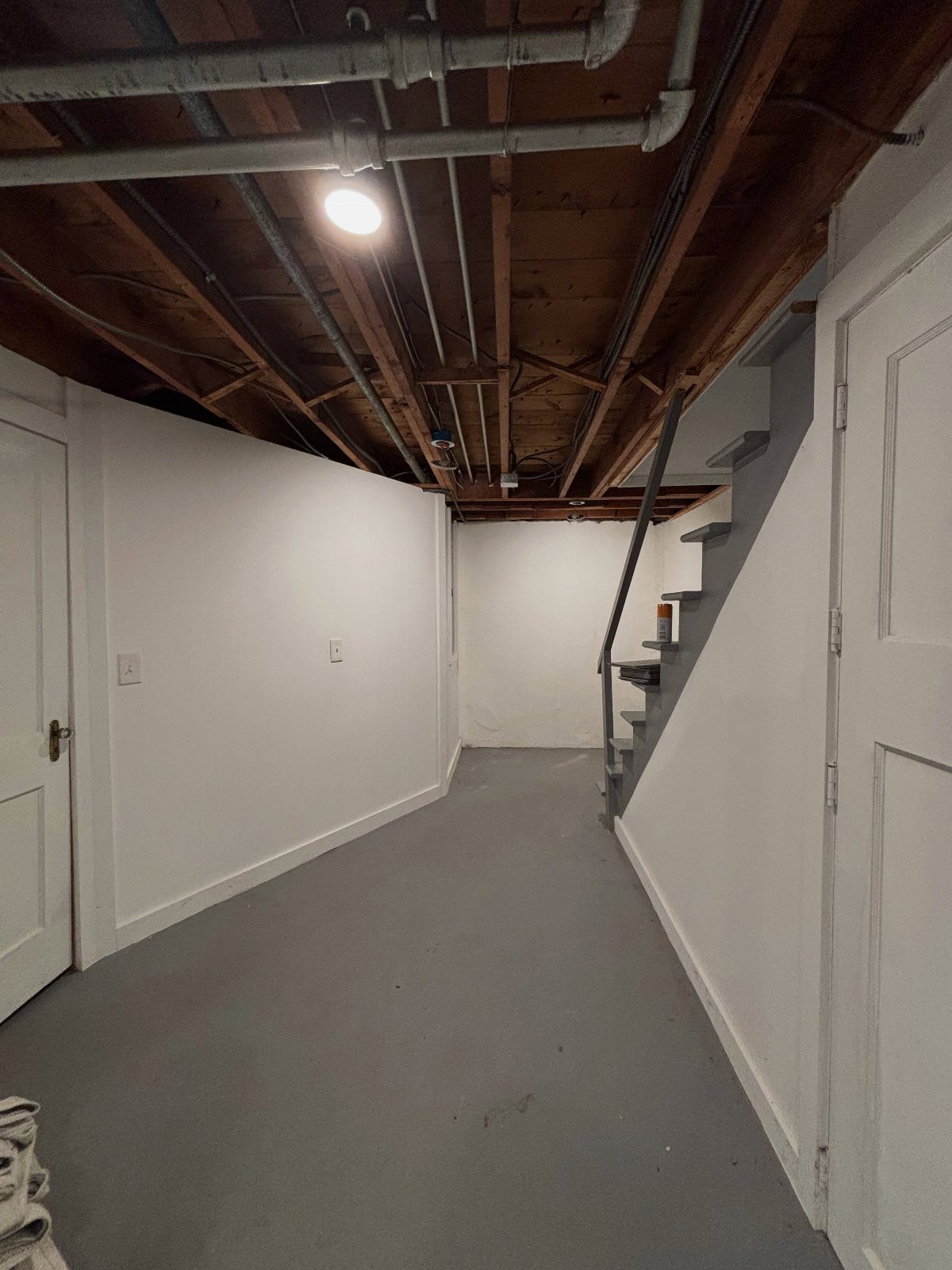 Exposed wooden joist ceiling with pipes in a white walled basement room