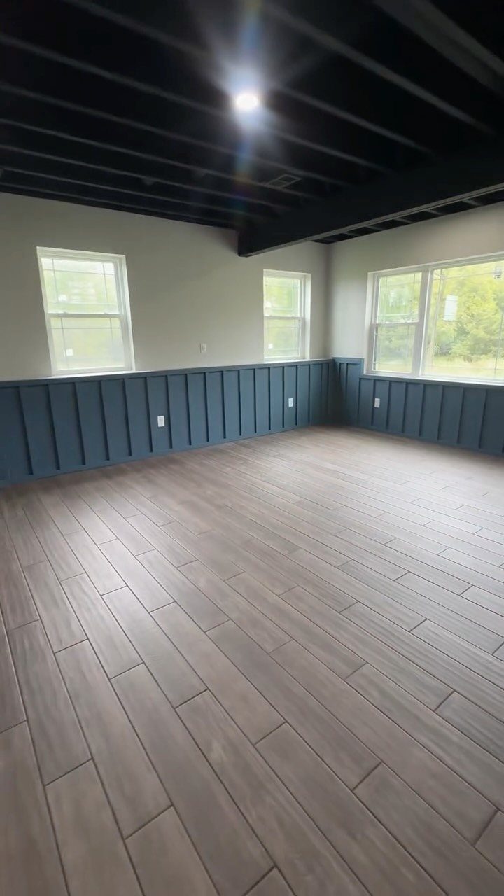 Black painted exposed ceiling joists in a room with grey floors and blue wainscoting