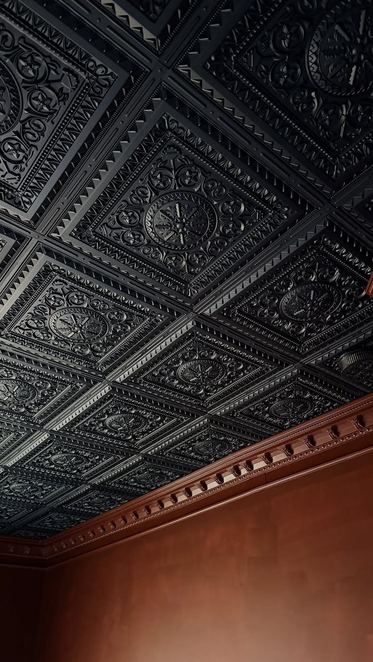 Ornate black tin ceiling tiles with embossed patterns and decorative wooden crown molding.