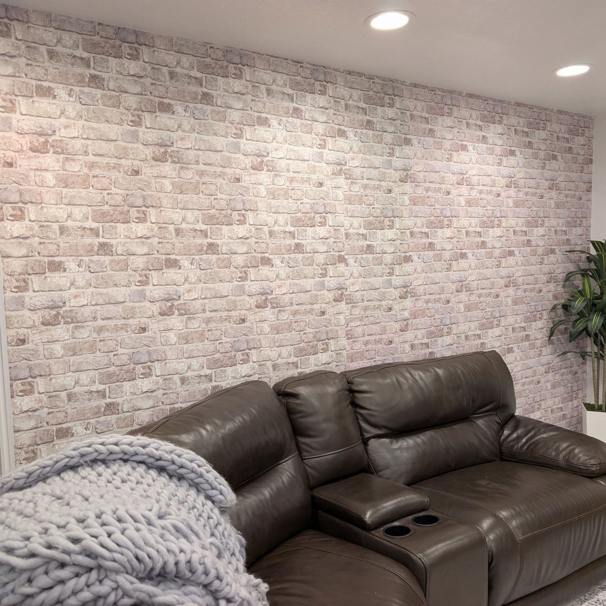 Brown leather sofa against a light-colored faux brick accent wall in a room.