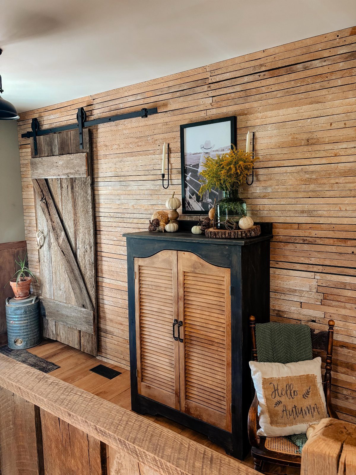Wooden plank wall with a sliding barn door and black rustic cabinet.