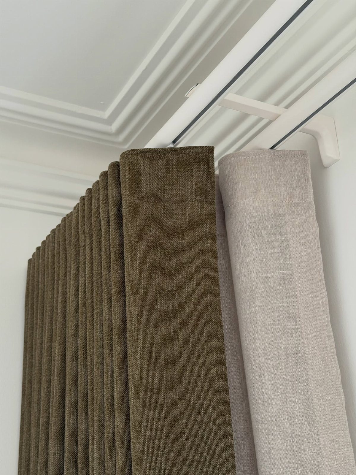Olive green and beige textured curtains hanging from a white ceiling track.