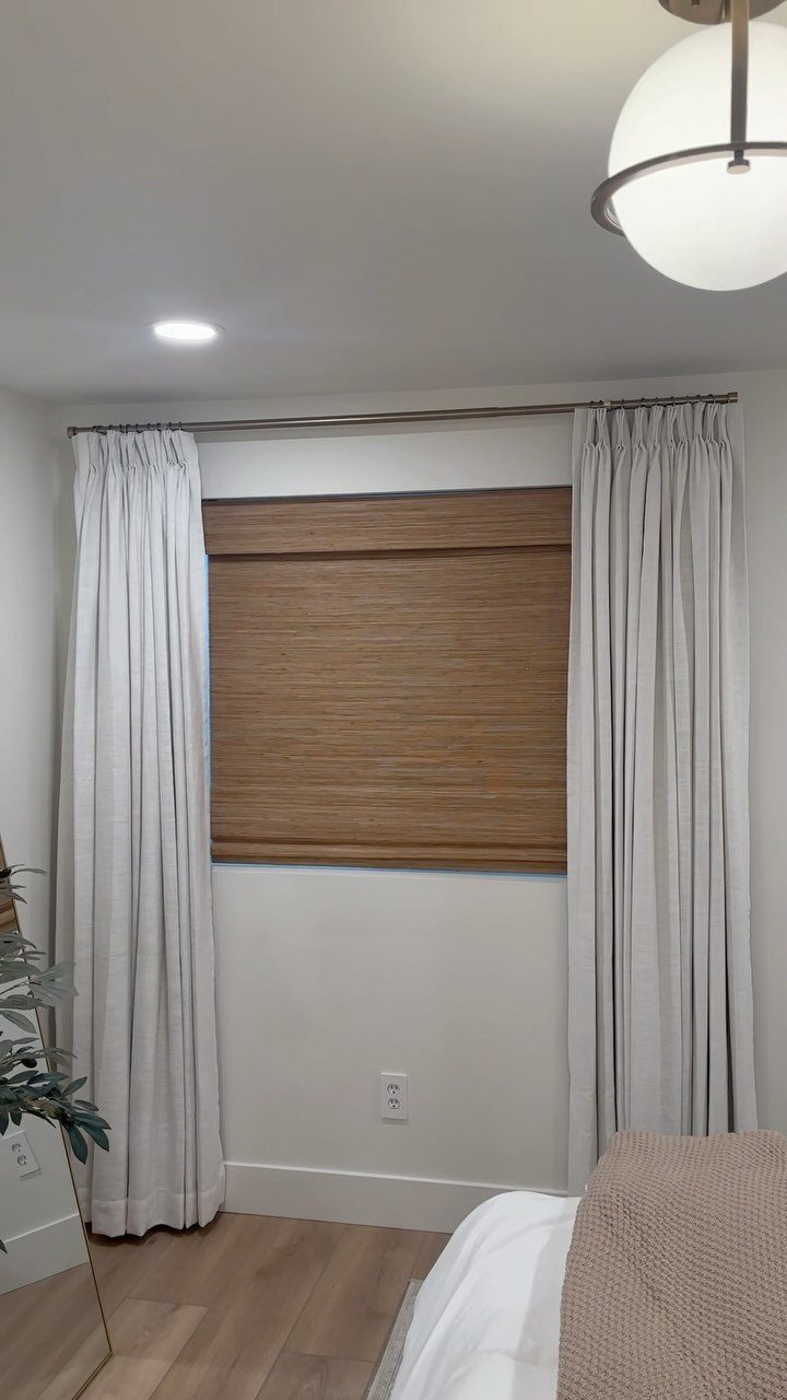 Brown woven bamboo shades and light grey curtains on a bedroom window