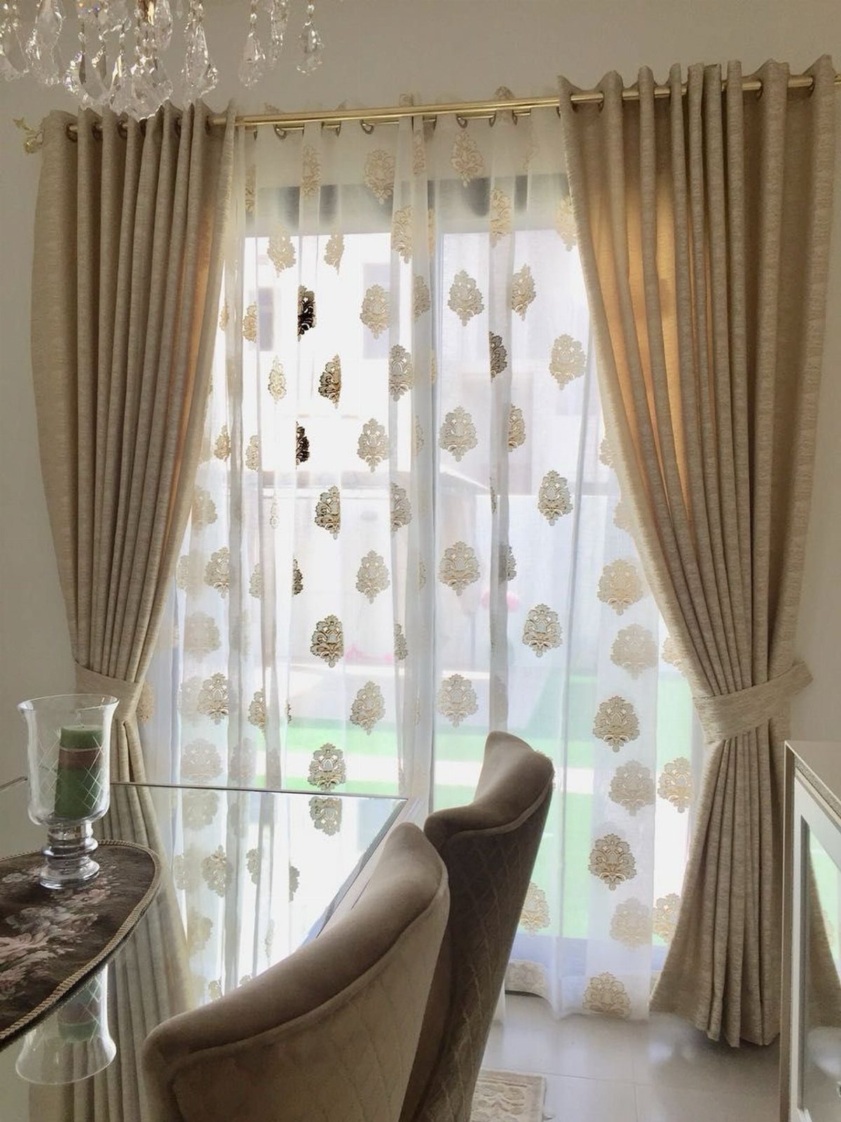 White sheer drapes with gold patterns framed by beige curtains in a dining room