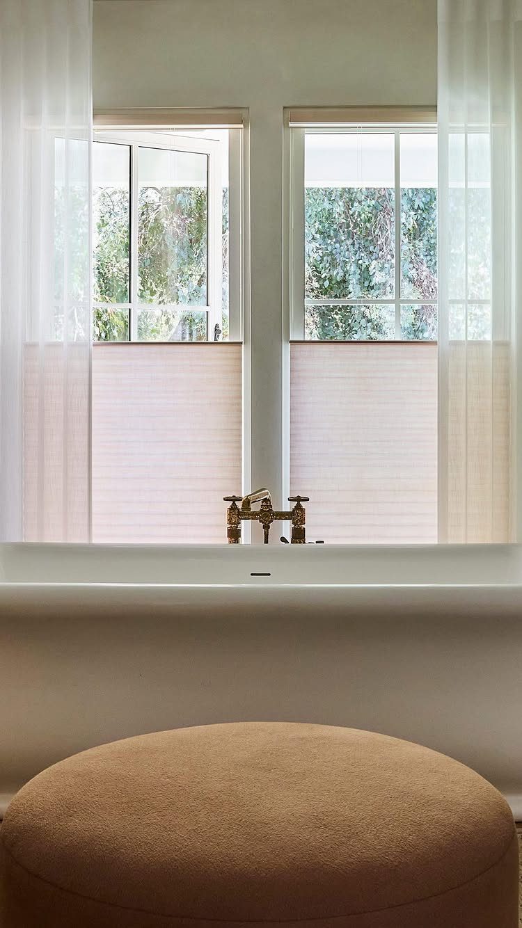 Beige top-down bottom-up cellular shades on two windows with sheer white curtains.