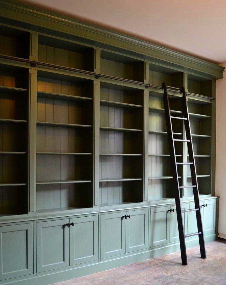 Dark green built-in bookshelves with a black rolling ladder in a home office.