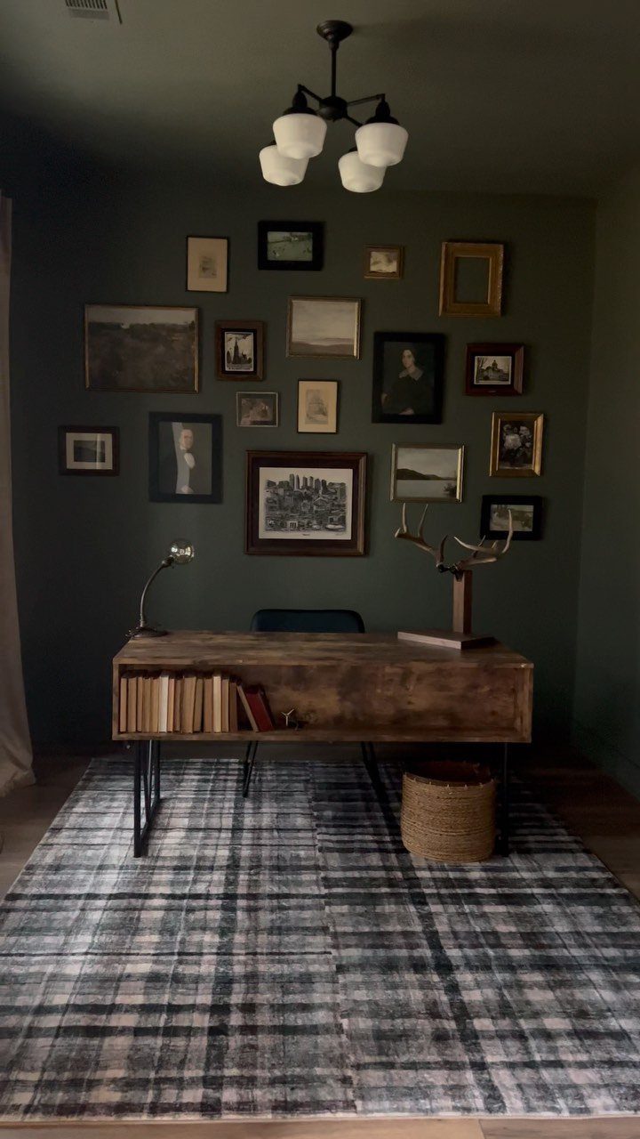 Dark green home office with a wooden desk and a gallery wall of art.
