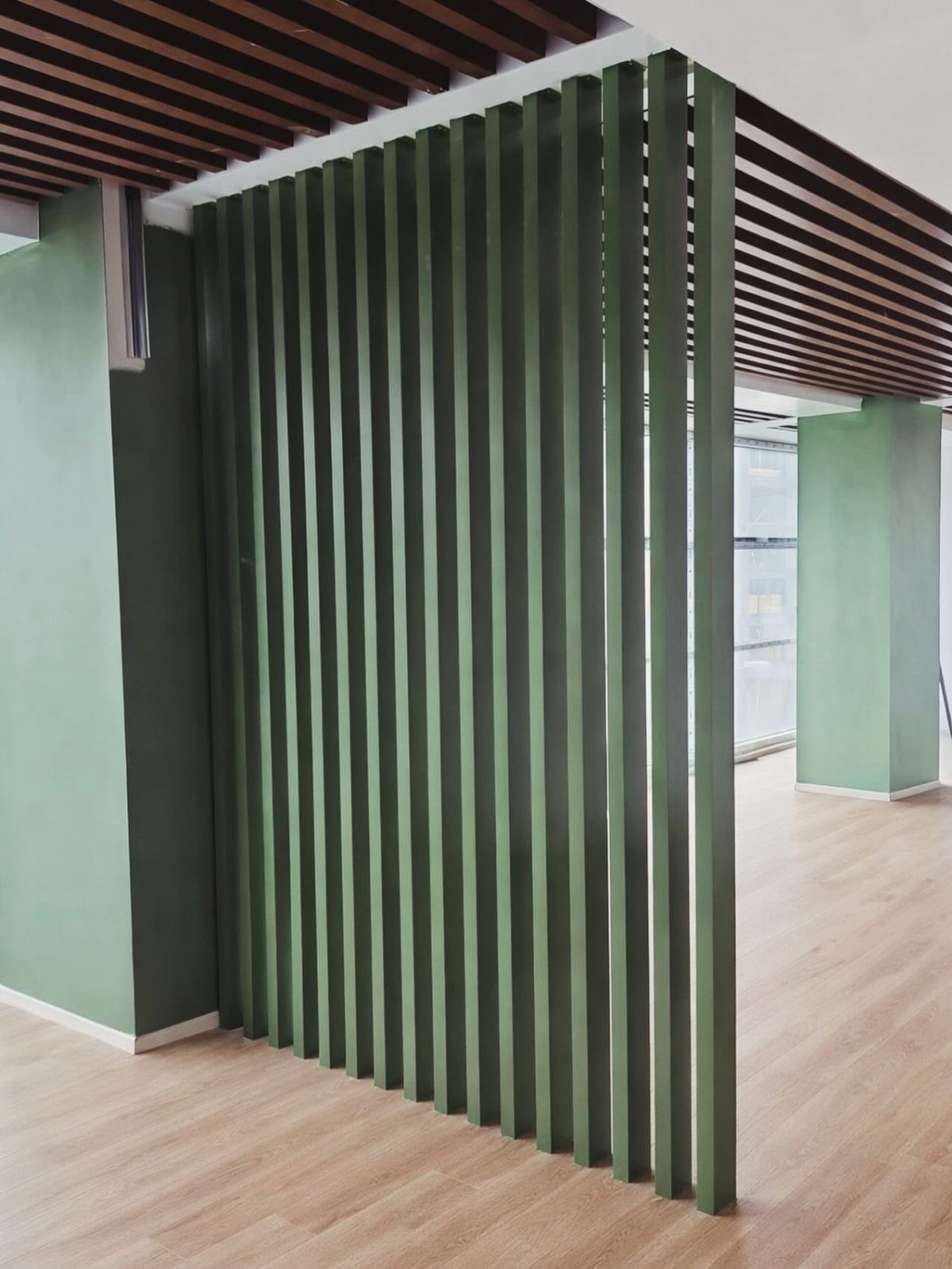 Dark green vertical slatted room divider in a modern office with wooden floors.