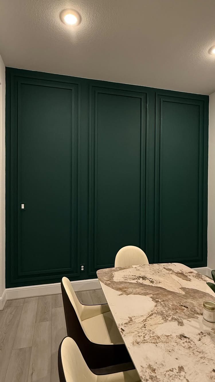 Dark green paneled wall behind a marble table with cream chairs in a room.