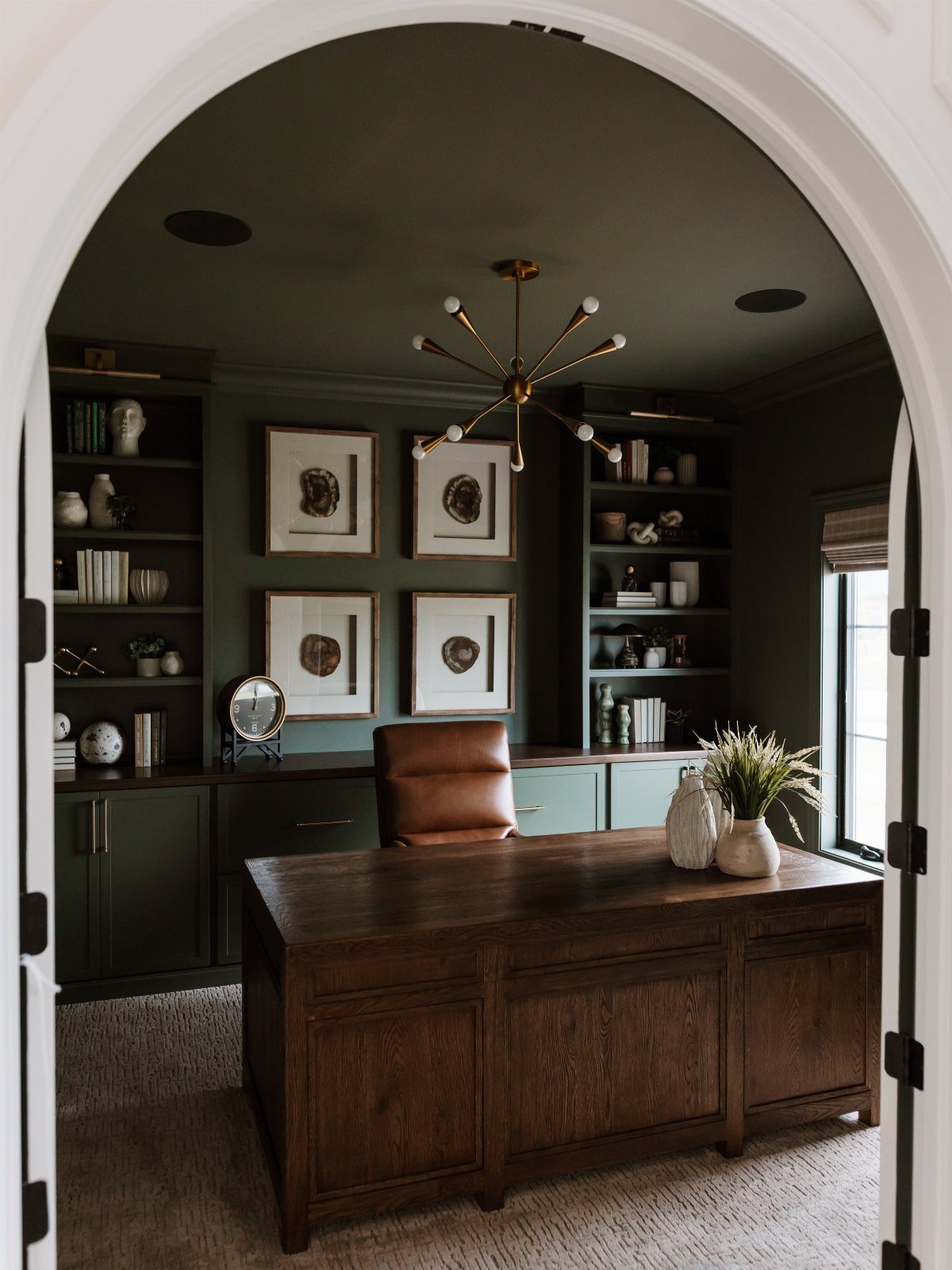 Dark green home office with a wooden desk and gold sputnik chandelier