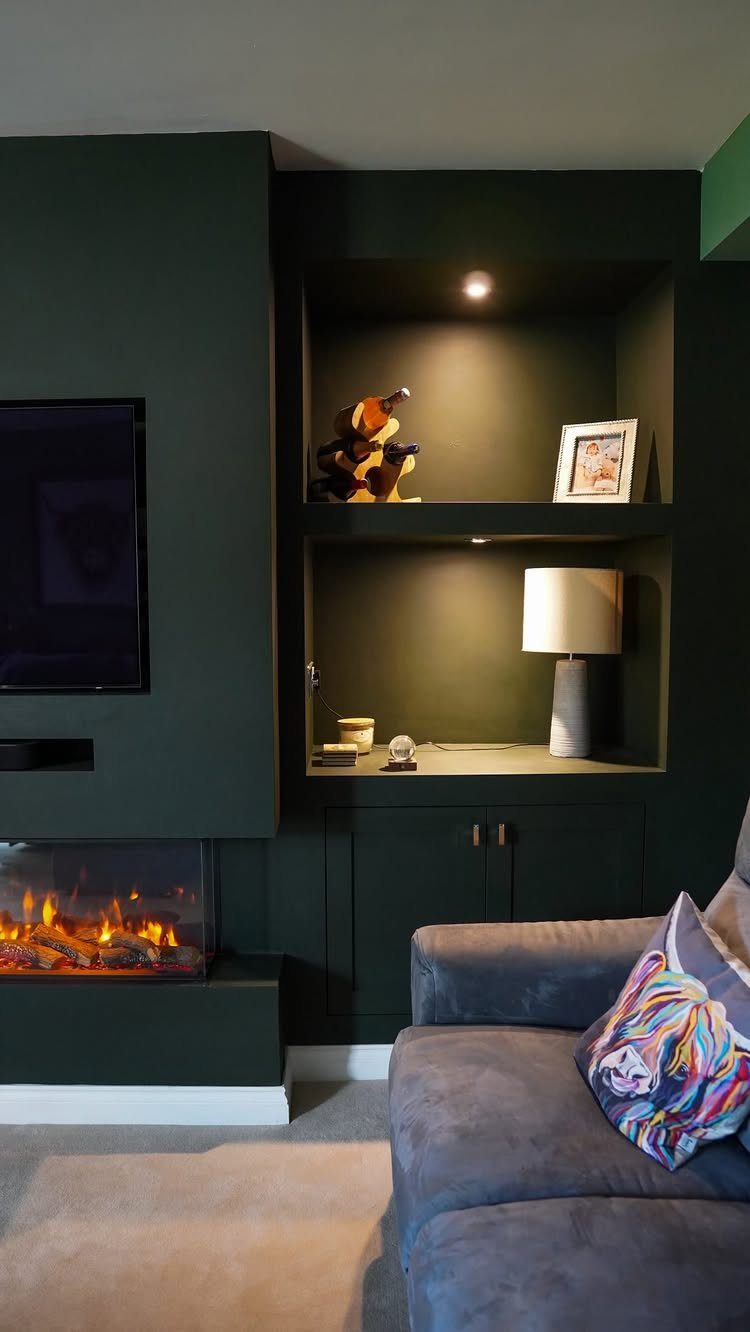 Dark green feature wall with electric fireplace, mounted TV, and built-in shelving alcove.