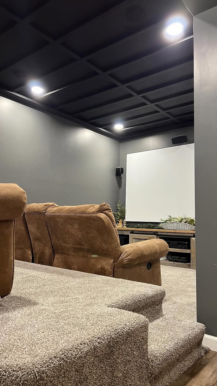 Black coffered ceiling in a home theater with brown reclining seats and screen.