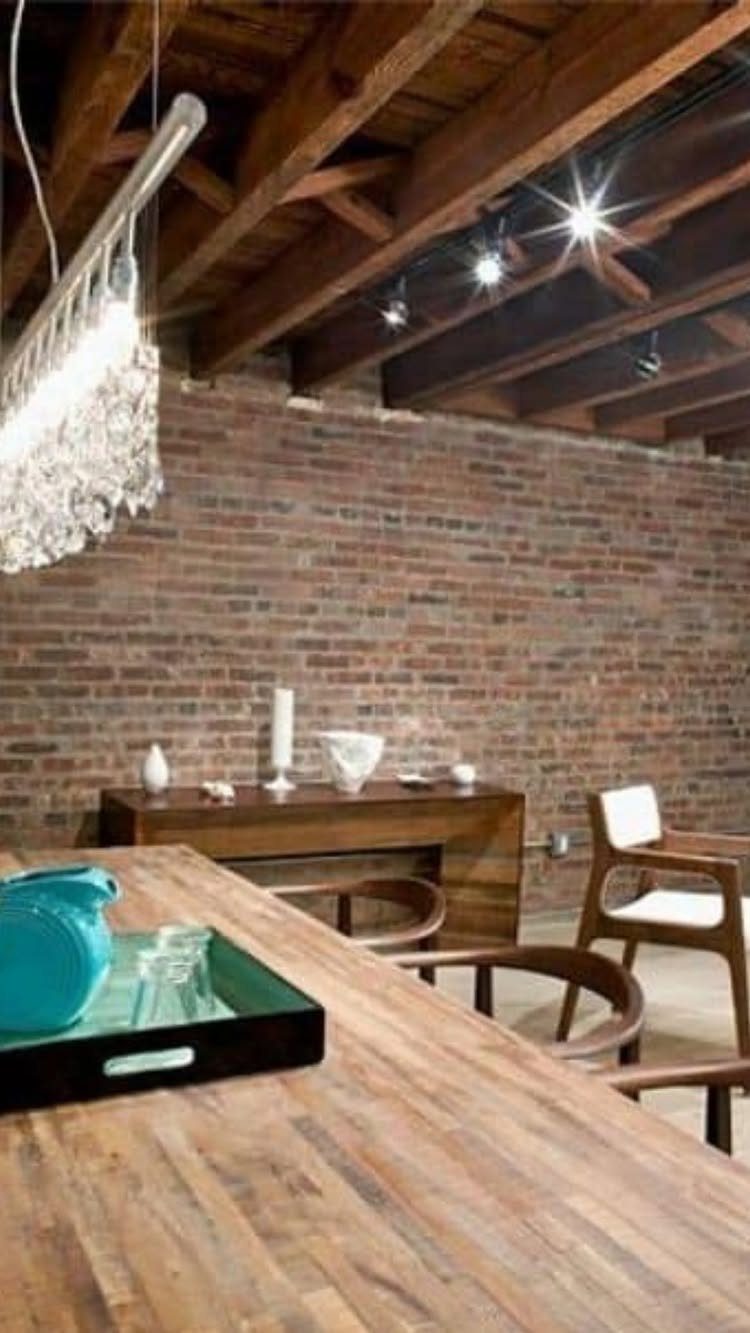 Exposed wooden beam ceiling with track lighting above a brick wall and dining area.