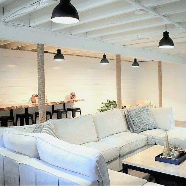 White painted exposed basement ceiling with black pendant lights over a modern living room