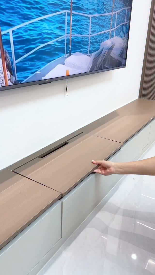 Hand lifting a wooden panel on a sleek media console under a TV.