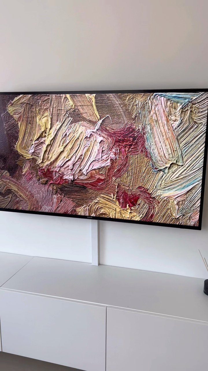 Flat-screen TV displaying a colorful abstract painting above a white minimalist console