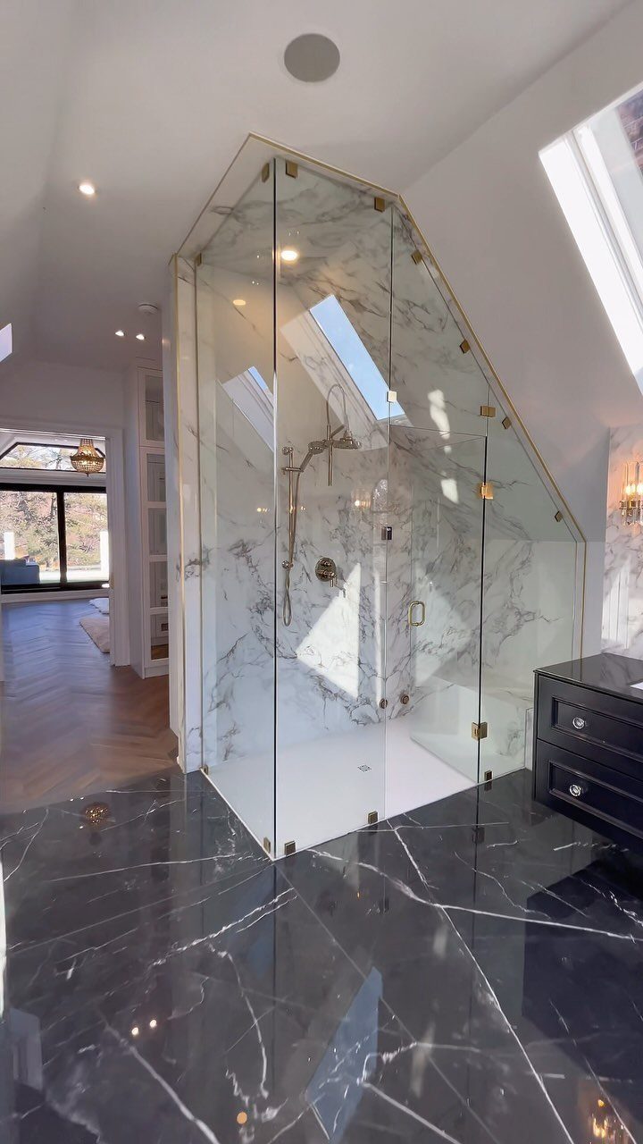 Modern attic bathroom with white marble shower, black marble floors, and a skylight.