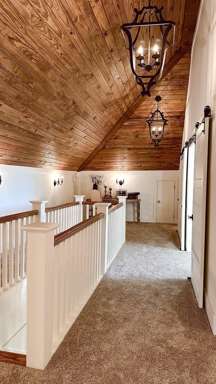 Finished attic hallway with sloped wood ceiling, white railings, and lantern chandeliers.