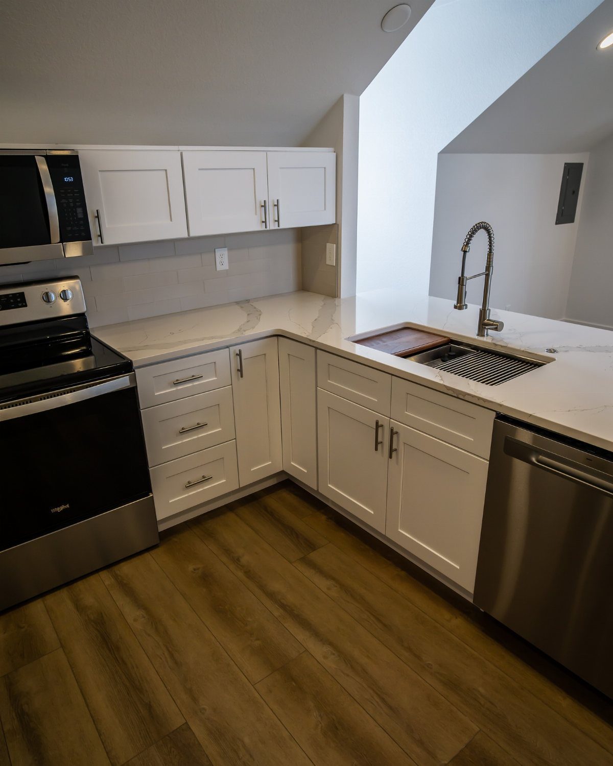 Modern white kitchen with marble countertops and wood floors under a sloped ceiling.