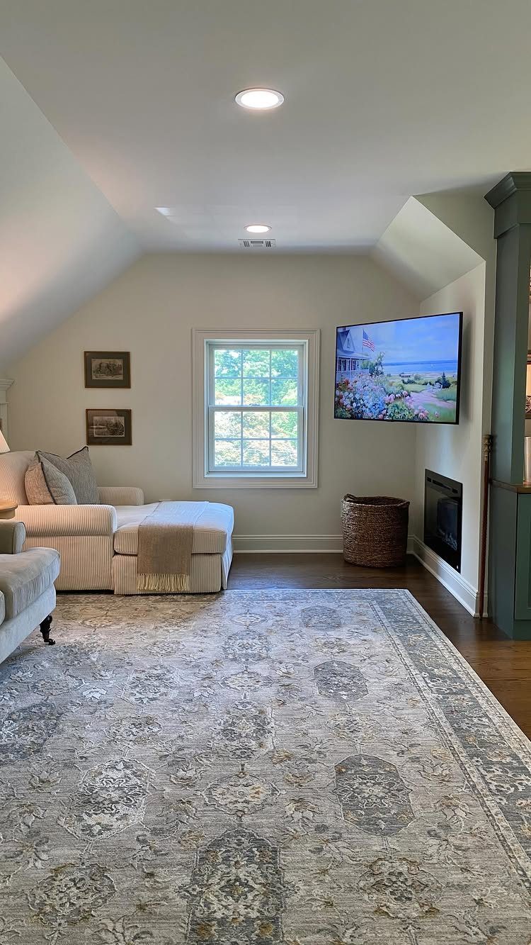 Finished attic living room with sloped ceilings, beige sofa, and patterned area rug.
