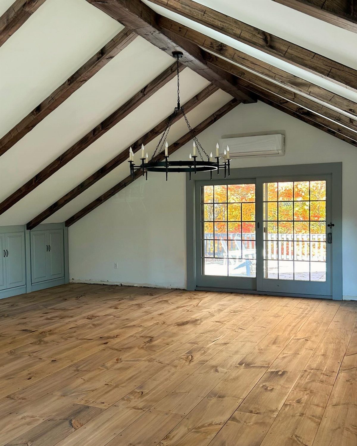 Finished attic room with exposed wooden beams, wood flooring, and grey French doors.