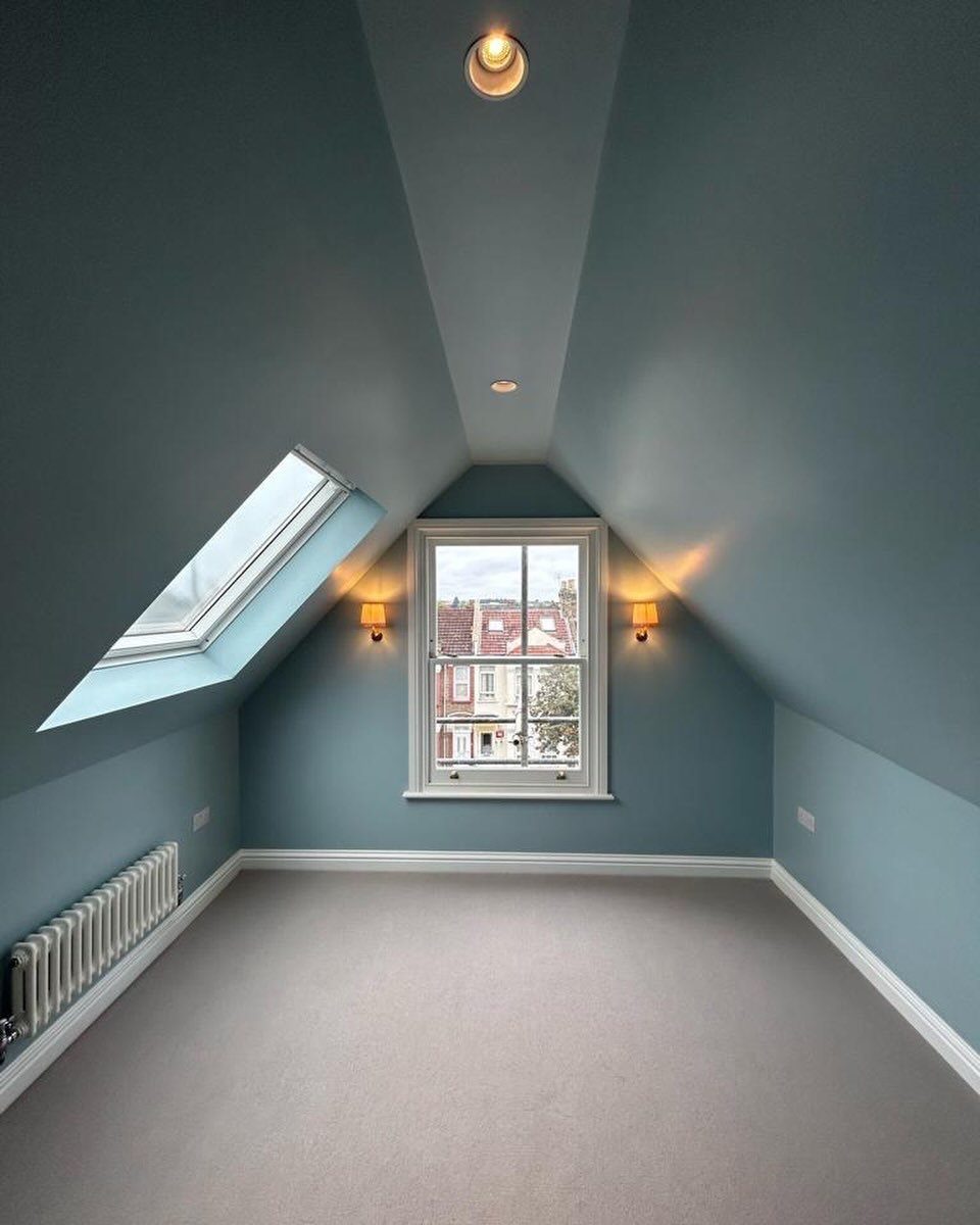 Empty blue attic room featuring a skylight and a central window for natural light.