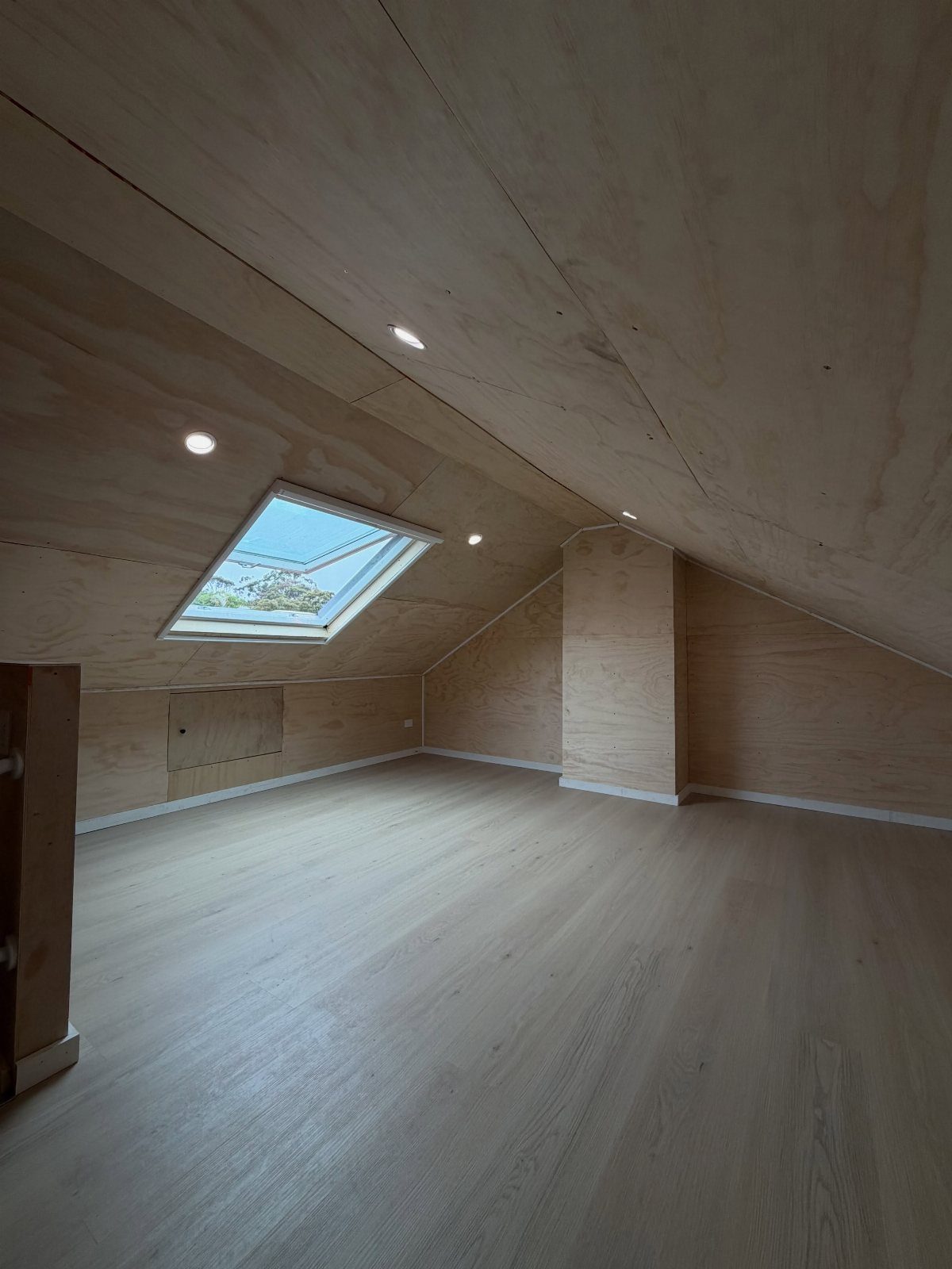 Light grey wood-plank flooring in an empty attic with wooden walls and skylight.