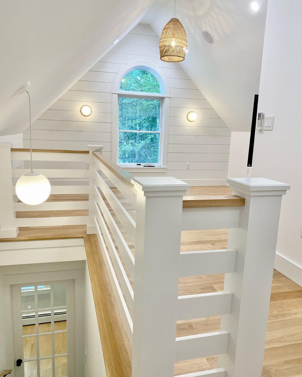 Bright attic room with white shiplap walls, light wood floors, and arched window.