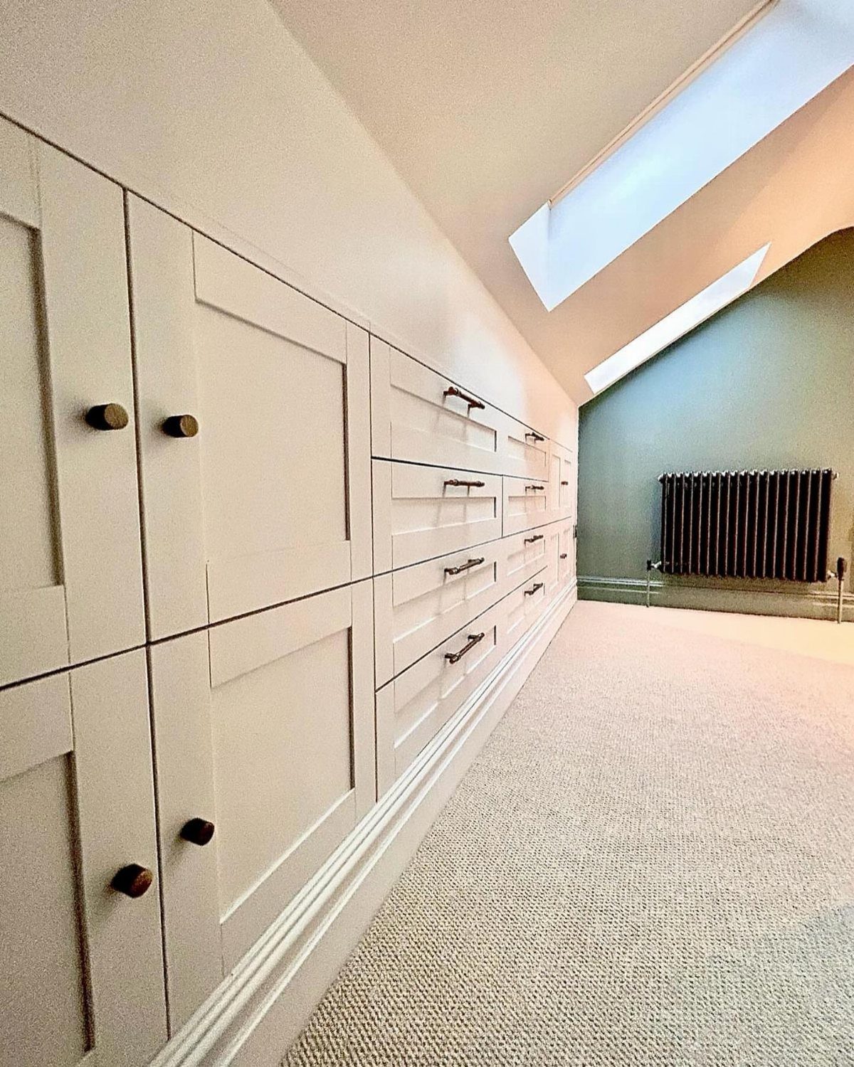 White built-in storage cabinets and drawers under a sloped attic ceiling with skylight.