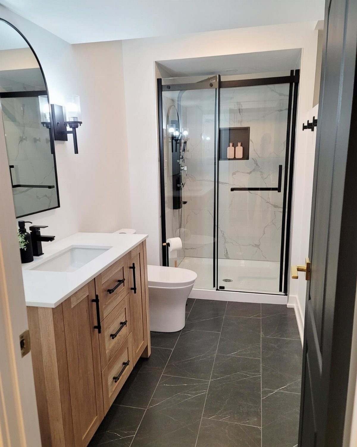 Modern bathroom with light wood vanity, white toilet, and marble shower enclosure.