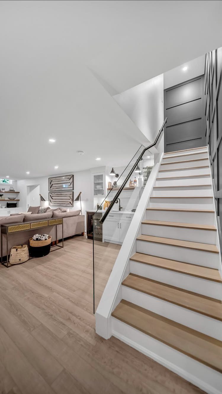 Modern finished basement with light wood floors, white stairs, and a grey sofa.