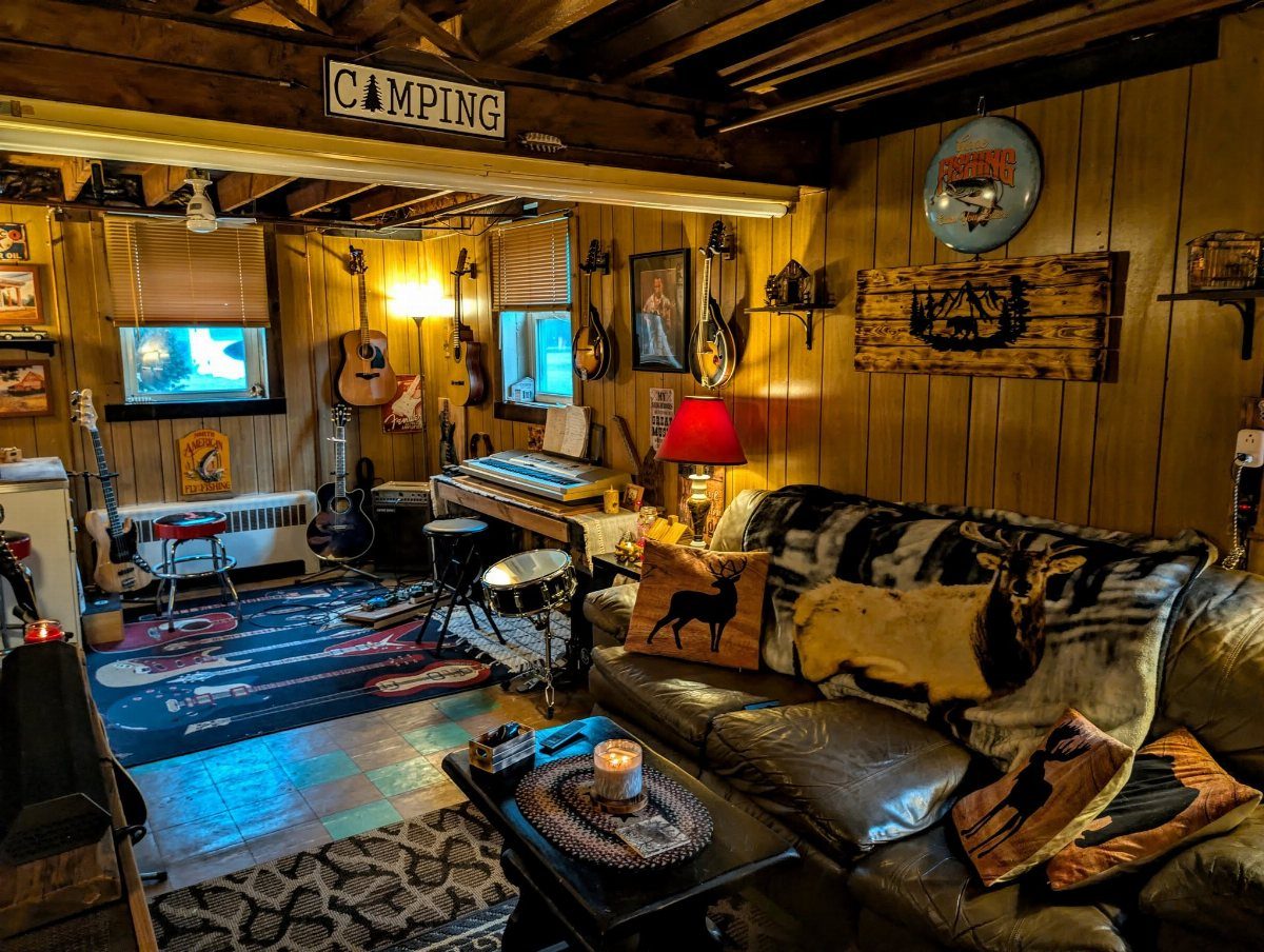 Rustic wood-paneled man cave with leather sofa, deer pillows, and musical instruments.