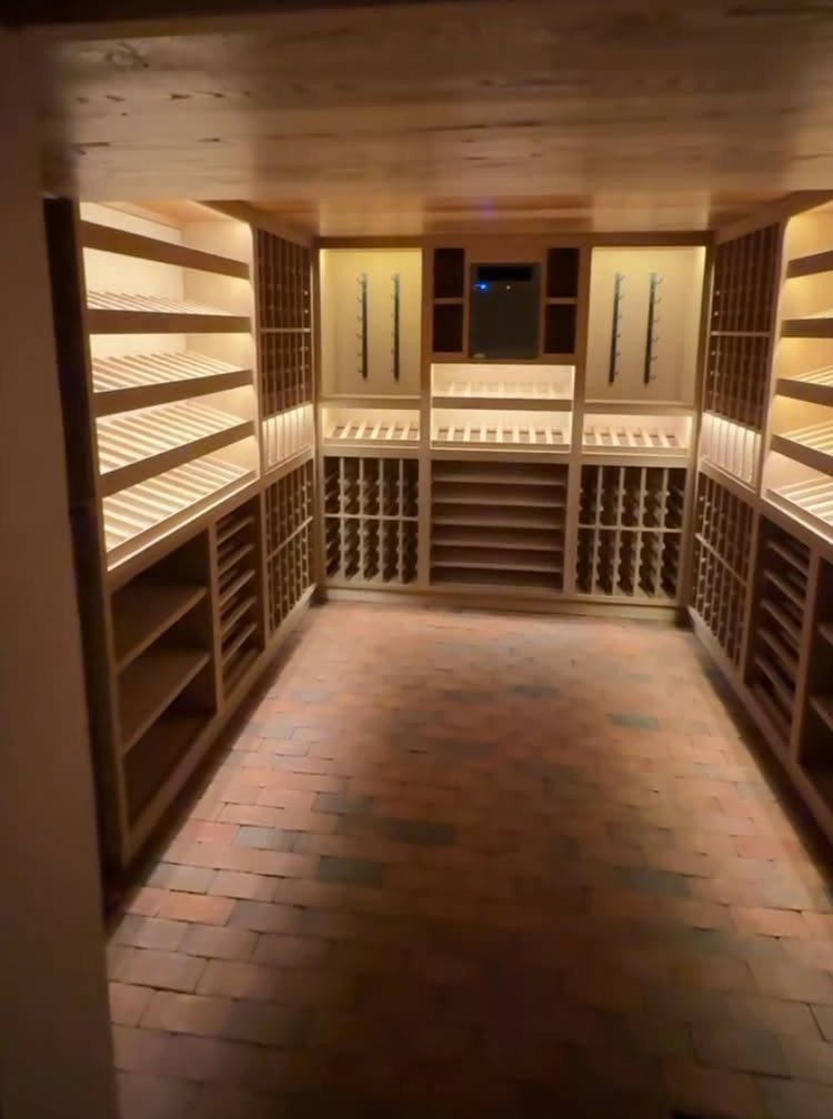 Wooden wine racks lining the walls of a room with brick flooring.
