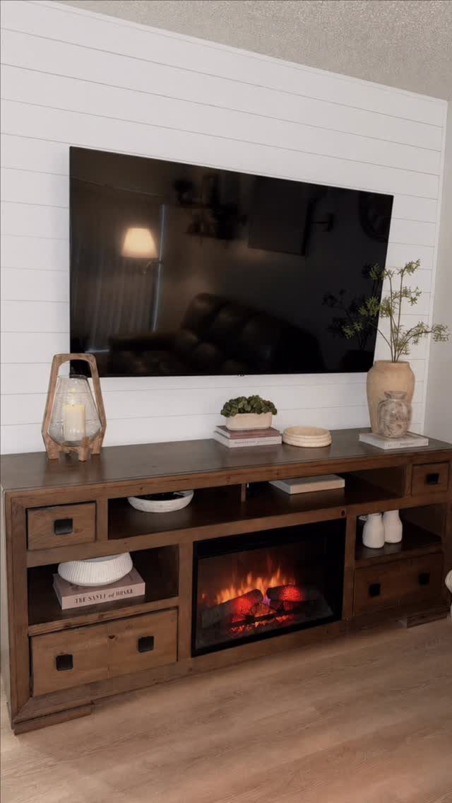 White shiplap accent wall with a mounted TV above a wooden electric fireplace console