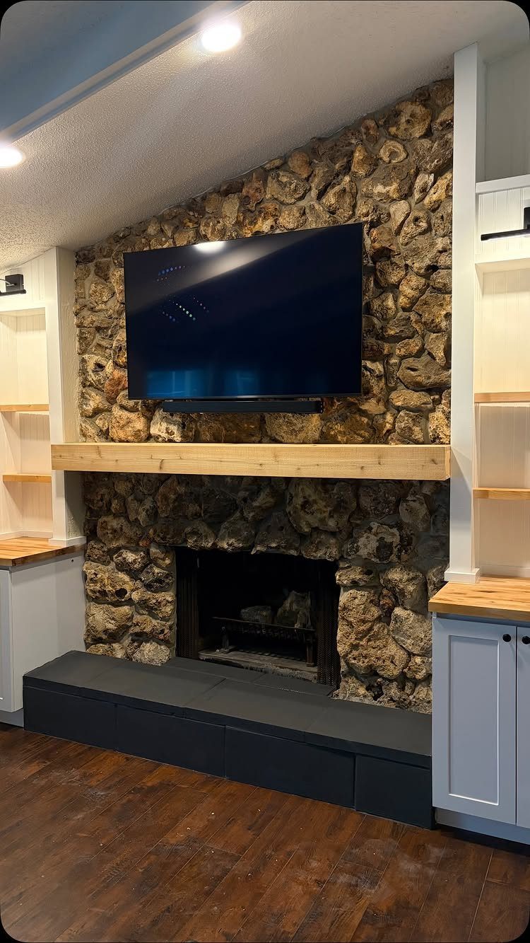 Rustic stone fireplace with a wooden mantel and a television mounted above it.