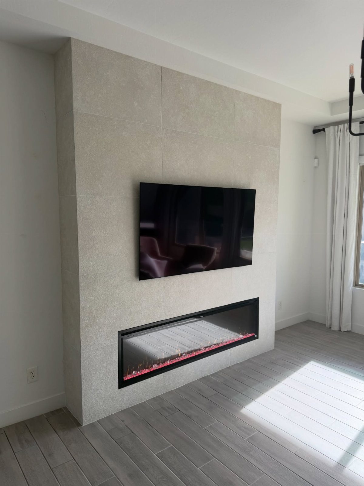 Floor-to-ceiling beige tile wall with a mounted TV and linear electric fireplace.