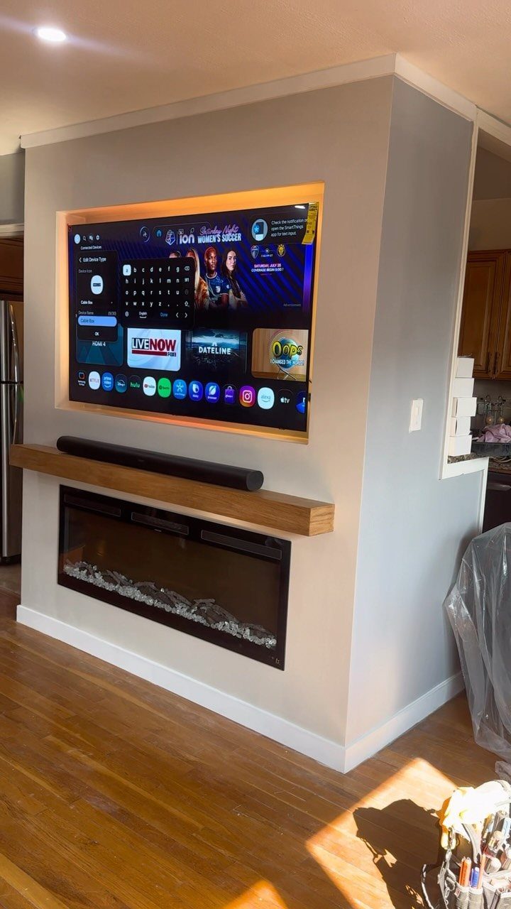 Recessed television with orange backlight above a wooden mantel and linear electric fireplace.