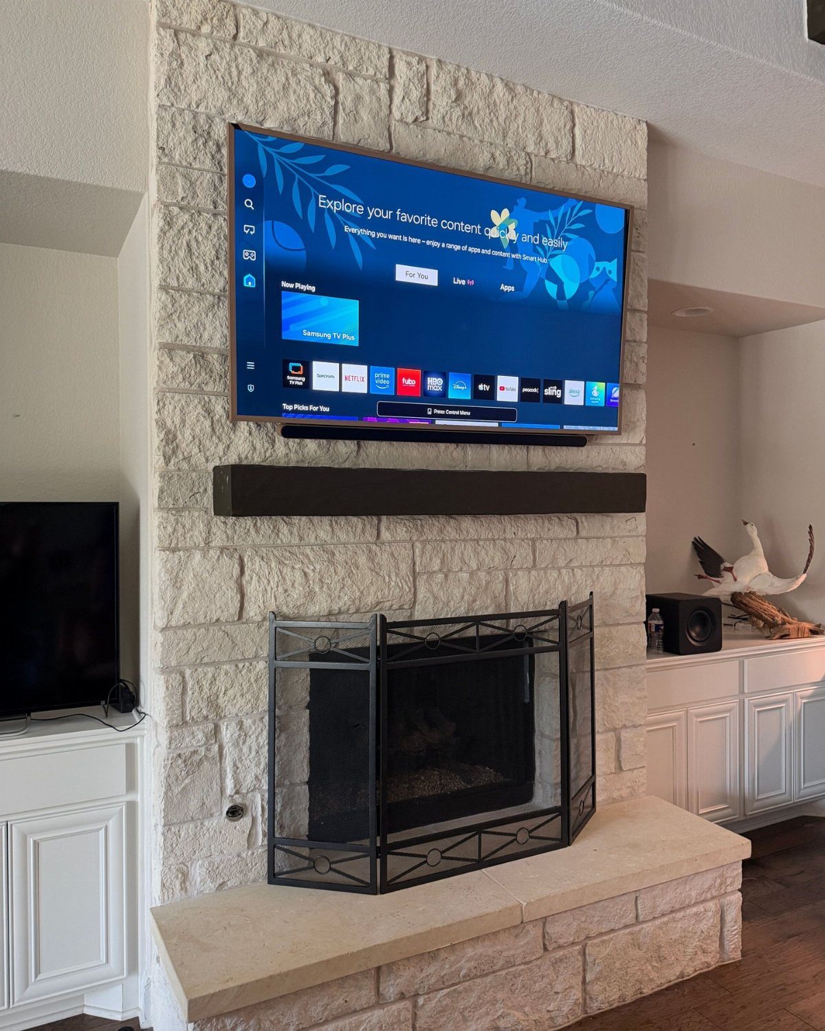 Stone fireplace surround with a dark wood mantel and television mounted above it.