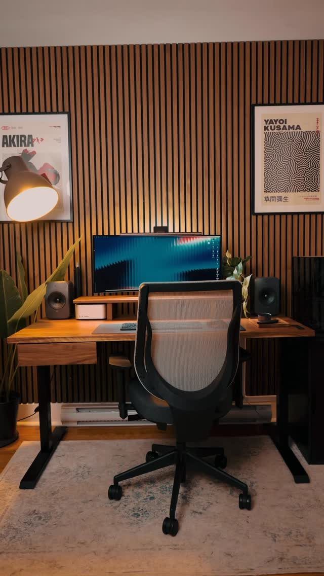 Gaming desk setup with a mesh chair against a vertical wooden slat wall.