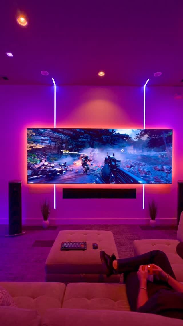 Modern gaming room with purple ambient LED lighting and a large wide-screen television.