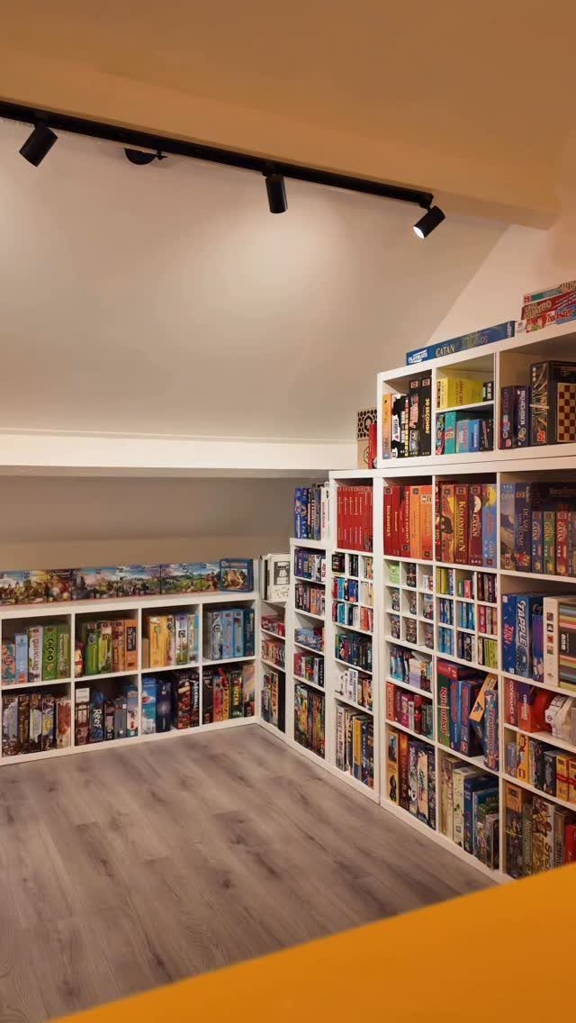 White bookshelves filled with board games in a room with grey wood floors.