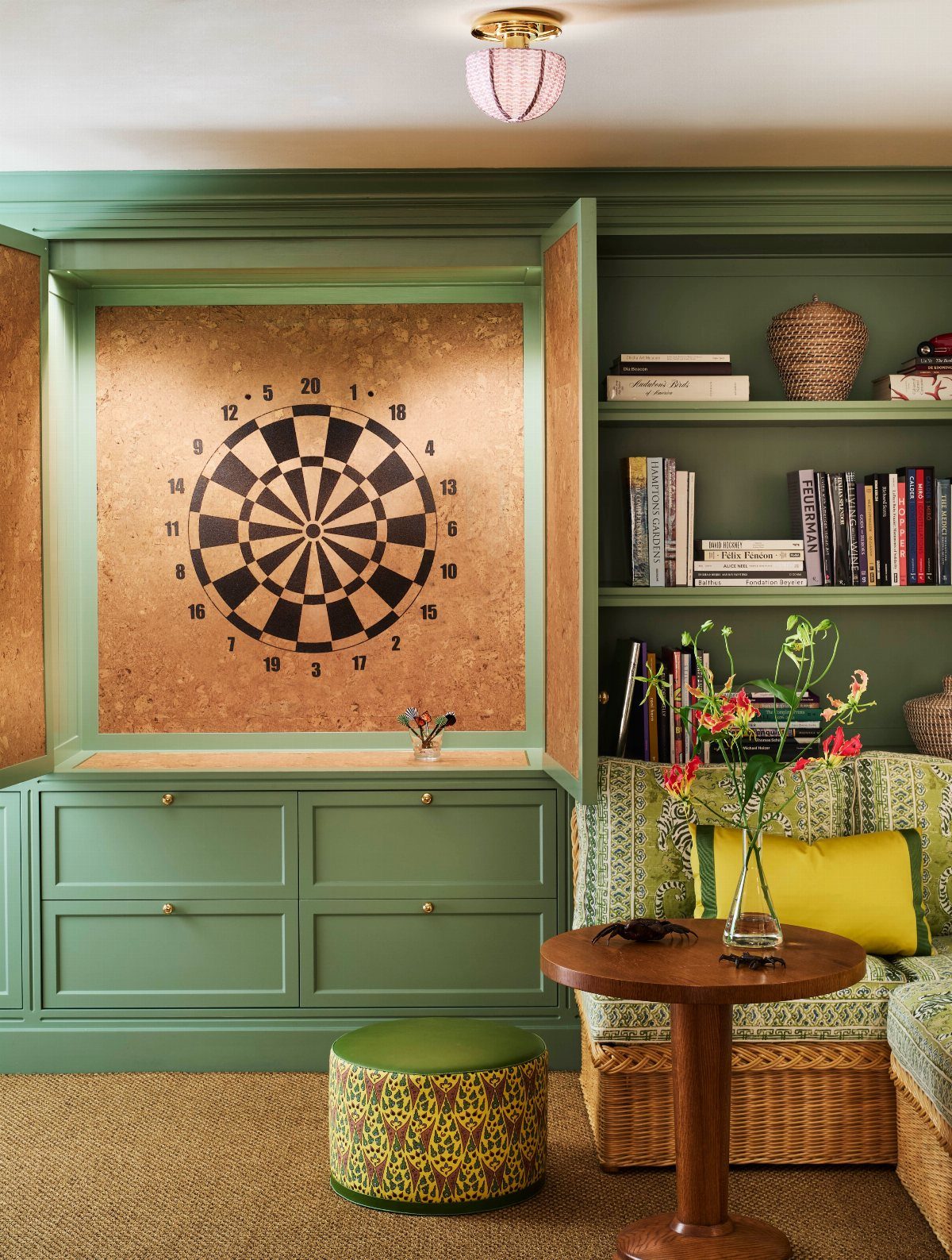 Green game room with a built-in dartboard, bookshelf, and patterned furniture.